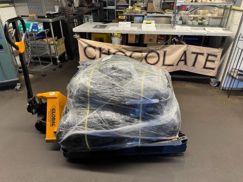 Satu palet karung yang dibungkus plastik wrap di atas troli palet, di dalam gudang buyer.